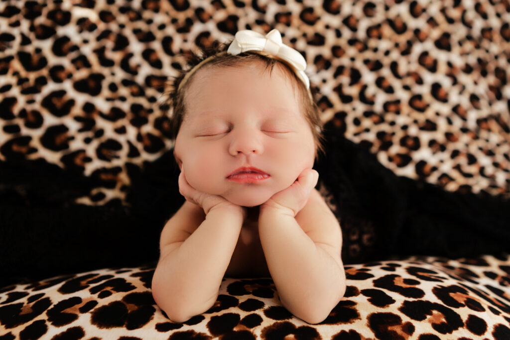 newborn baby girl with her chin in her hands, resting on her elbows in froggy pose
